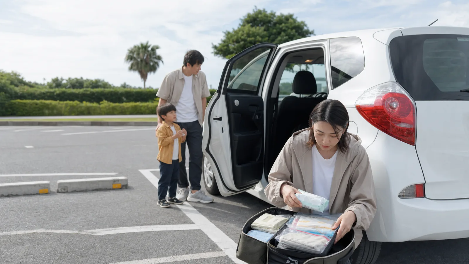 一家三口將租車停妥後,家長在車旁整理濕紙巾、替換衣物與夾鏈袋等車上備用品